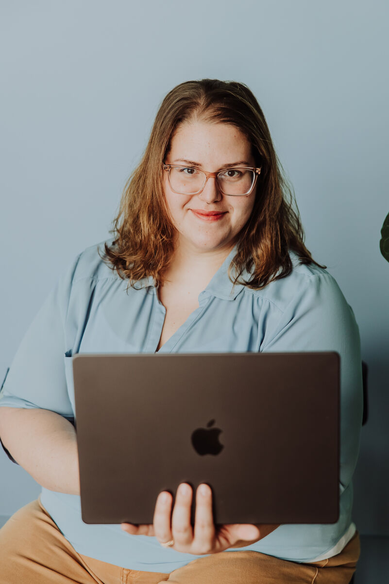 Jenn holding her open MacBook with a subtle smile