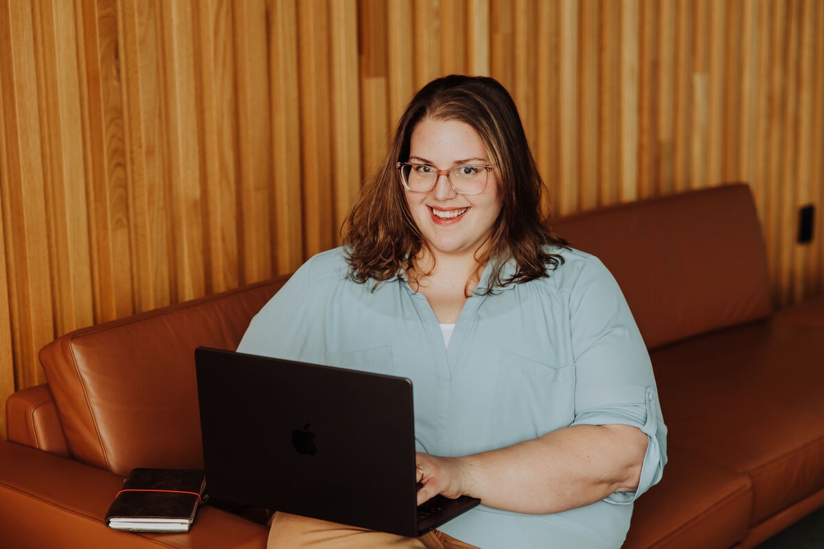 Jenn smiling on a leather couch with her MacBook